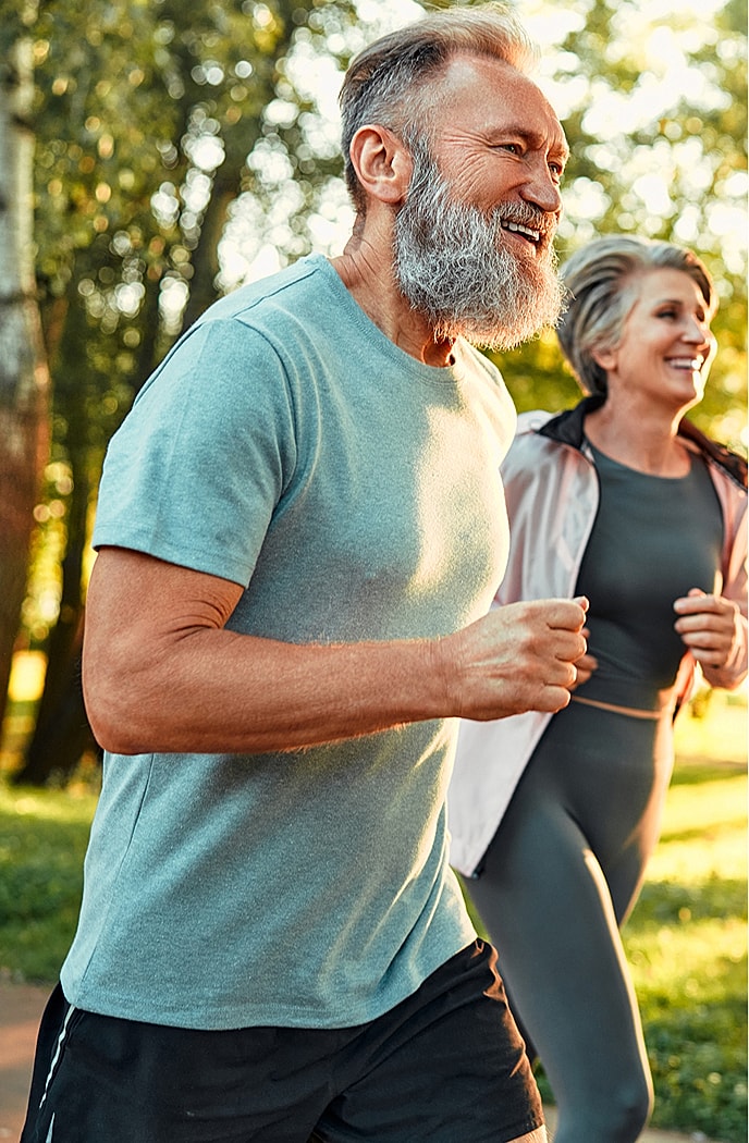 Happy seniors jogging outdoors in sunlight.
